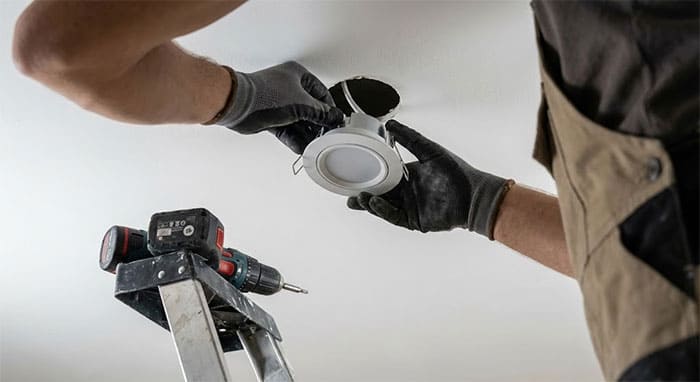 Người thợ đang thực hiện thao tác bóp tai lò xo để đưa đèn vào lỗ khoét trần thạch cao