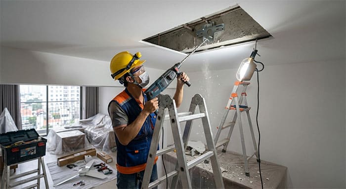 Kỹ sư điện thực hiện thao tác khoan xuyên thạch cao để bắt bích thép quạt trần vào dầm bê tông