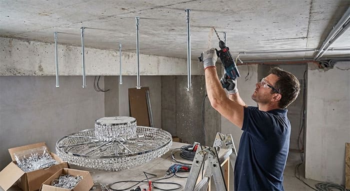 Kỹ thuật viên đang gia cố ty treo lên trần bê tông trước khi lắp đèn mâm pha lê